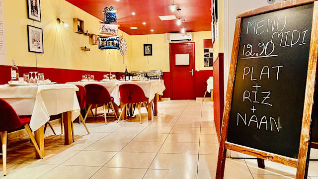 Intérieur de restaurant chaleureux avec des tables bien dressées, un menu spécial déjeuner à 12,20 € proposant un plat, du riz et du naan, et des murs décorés de photos encadrées.