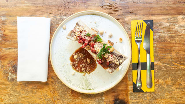Tagliata di manzo con salsa ricca, guarnita con erbe fresche e noci sbriciolate, accompagnata da ingredienti schiacciati.
