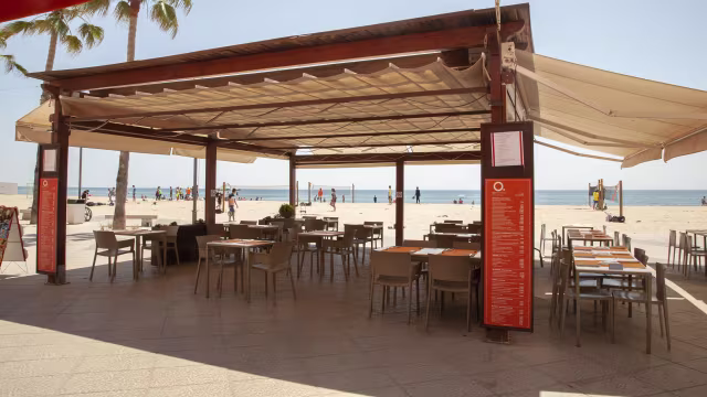 Restaurante al aire libre junto a la playa, con mesas organizadas y sillas modernas, ofreciendo un ambiente relajado y vistas al océano.