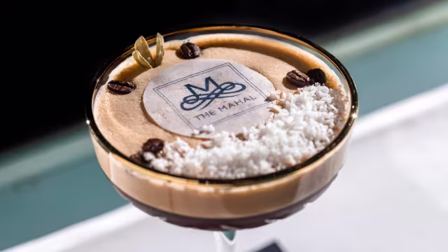 Coffee-flavored mousse topped with froth, shredded coconut, and whole coffee beans, resting on a rich chocolate layer.