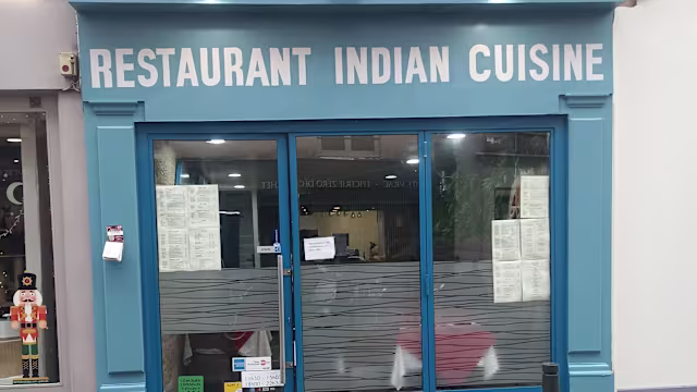 Extérieur d'un restaurant indien avec une façade bleue vive, une enseigne en lettres audacieuses et des menus affichés aux fenêtres, créant une atmosphère accueillante.