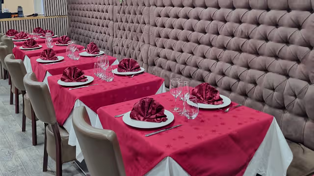 Mise en place élégante avec des tables recouvertes de nappes rouges, assiettes blanches soigneusement disposées et serviettes rouges pliées, créant une ambiance sophistiquée pour des occasions spéciales.