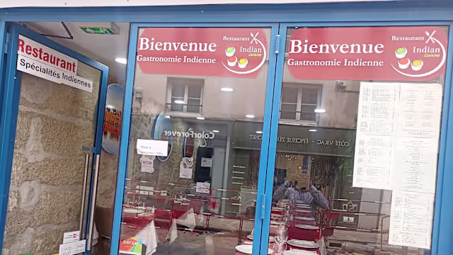 Restaurant indien avec de grandes fenêtres en verre, affichant des signes accueillants et une ambiance chaleureuse, suggérant une expérience décontractée.