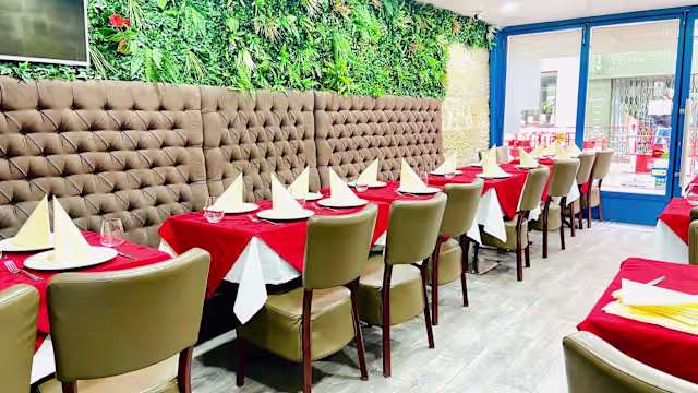 Intérieur du restaurant chaleureux et accueillant, avec des sièges en cuir marron et des nappes rouges vives, agrémenté de verdure luxuriante.