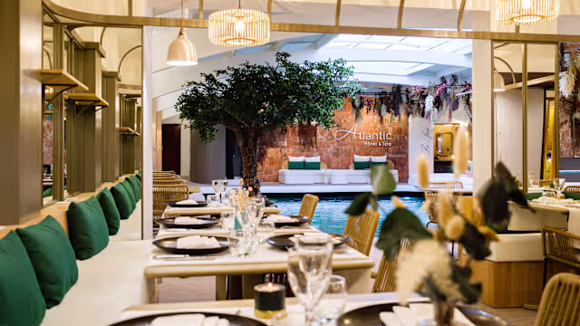 Intérieur de restaurant moderne et accueillant avec des tables en bois, des coussins verts confortables, et une ambiance tranquille grâce à une piscine et des œuvres d'art élégantes.