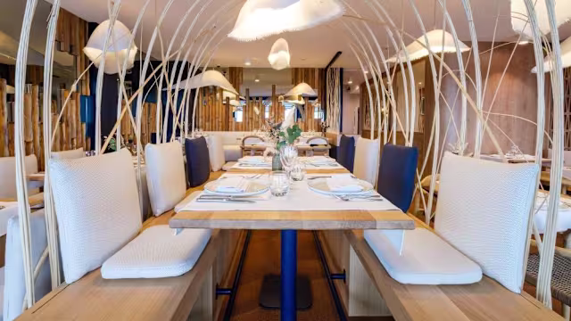 Intérieur de restaurant moderne avec un espace de restauration spacieux, tables en bois clair, sièges blancs confortables et éclairage unique en forme de nuages, créant une ambiance chaleureuse.