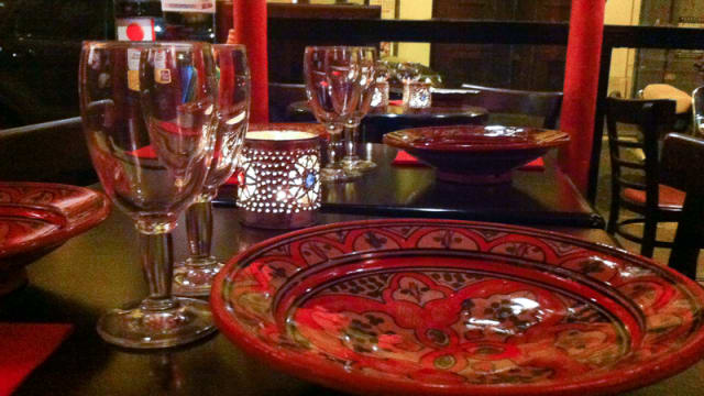 Ambiance chaleureuse d'un restaurant avec des tables décorées de plats rouges ornés de motifs floraux, de verrerie élégante et de bougeoirs délicats, créant une expérience de dîner accueillante.