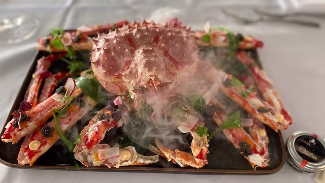 Indrukwekkend zeevruchtengerecht met een grote stekelige krab in het midden, omringd door prachtig gerangschikte krabbenpoten in heldere oranje en rode tinten, met hints van wit vlees. Verse kruiden en kleurrijke garneringen zoals radijsjes en eetbare bloemen verfraaien het geheel.