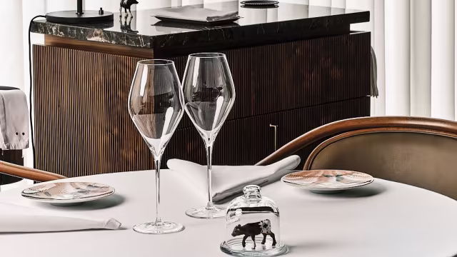 Ambiente raffinato di un ristorante moderno con tavolo lucido, bicchieri di vino eleganti e un centro decorativo sotto una campana di vetro.