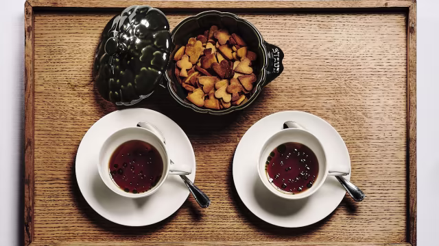 Due tazze di tè scuro e fumante, accompagnate da una ciotola di biscotti a forma di cuore, dorati e croccanti.