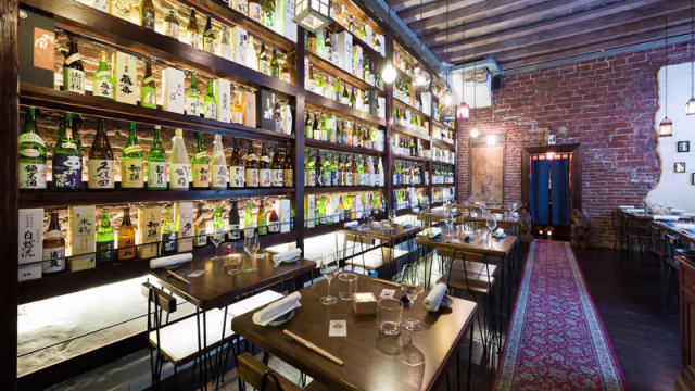 Interno di un ristorante elegante con un'atmosfera accogliente, caratterizzato da scaffali di sake e tavoli in legno dal design minimalista.