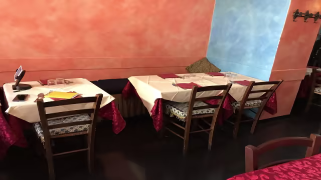 Interno di un ristorante accogliente con tavoli in legno, tovaglie bianche e decorazioni calde, che creano un'atmosfera informale e invitante.