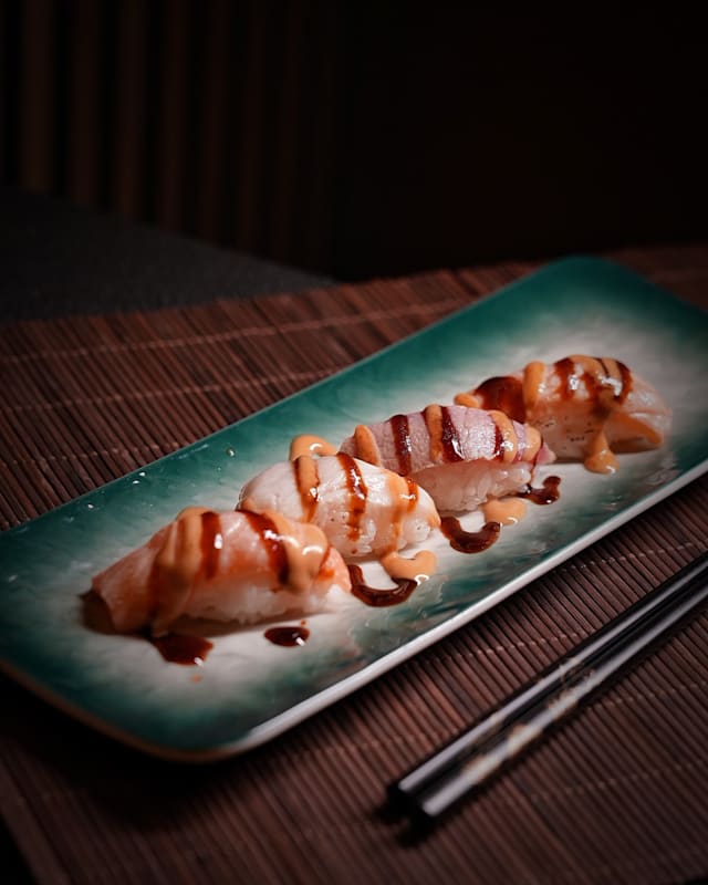 Tres piezas de sushi con una delicada rodaja de pescado sobre arroz, bañadas en una salsa cremosa de mayonesa y glaseado de soja dulce.