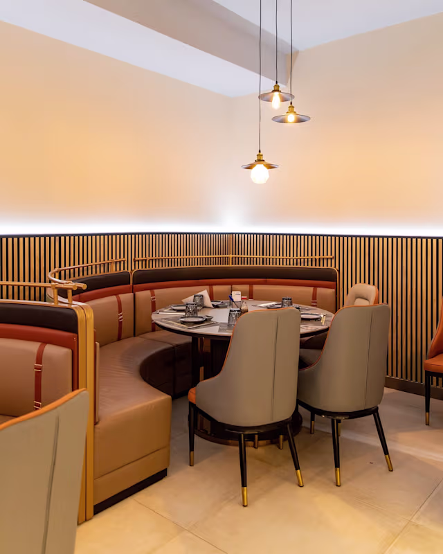 Interior de restaurante moderno con asientos en cabina, tonos cálidos y luces colgantes elegantes, creando un ambiente acogedor.