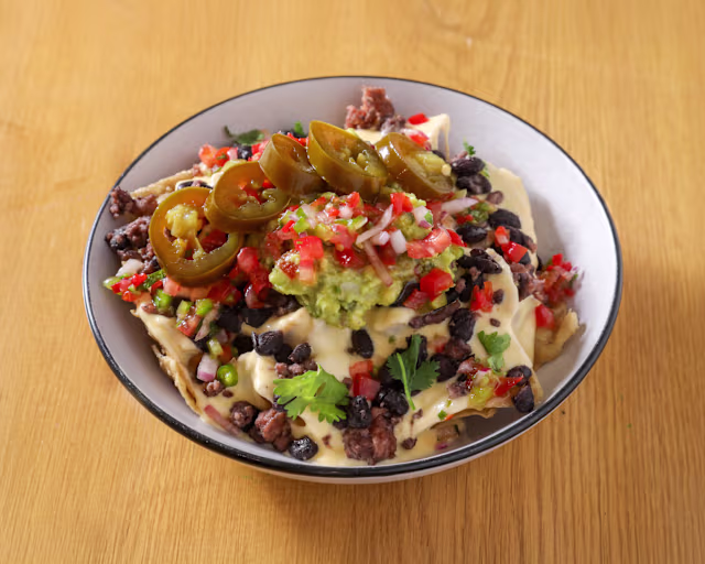 Nachos con carne molida, queso derretido, guacamole, pico de gallo fresco y rodajas de jalapeños.