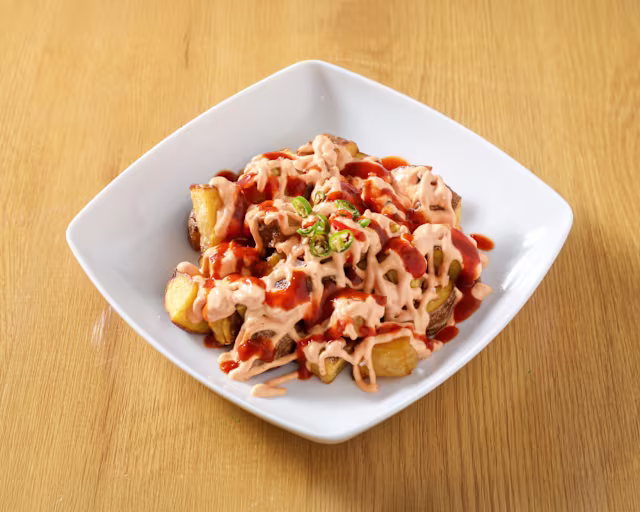 Porciones generosas de gajos de papa crujientes, con salsa cremosa y ketchup, decorados con hierbas frescas.