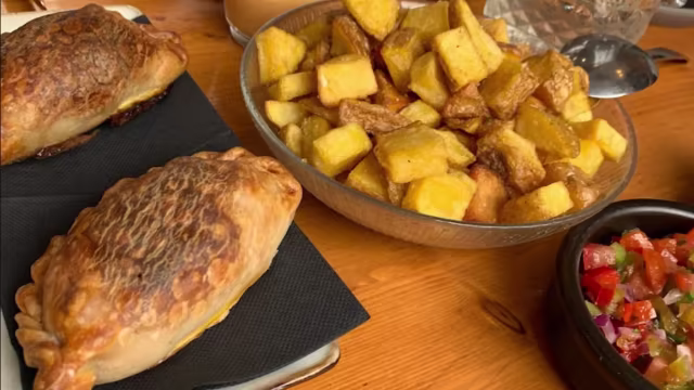 Empanadas doradas y crujientes rellenas de carne o queso, acompañadas de papas fritas en cubos y salsa fresca.