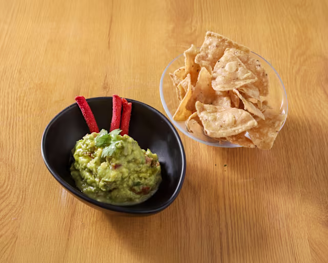 Guacamole cremoso con cilantro fresco y tiras de chile rojo, acompañado de totopos crujientes.