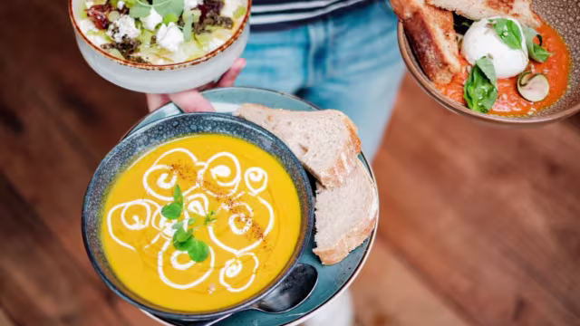 Een warme kom romige pompoensoep met een swirl van witte room en een snufje specerijen, vergezeld van verse kruiden en rustiek, krokant brood. Daarnaast een kleurrijk gerecht met een basis van geroosterde rode paprika, getopt met een gepocheerd ei en verse groenten.