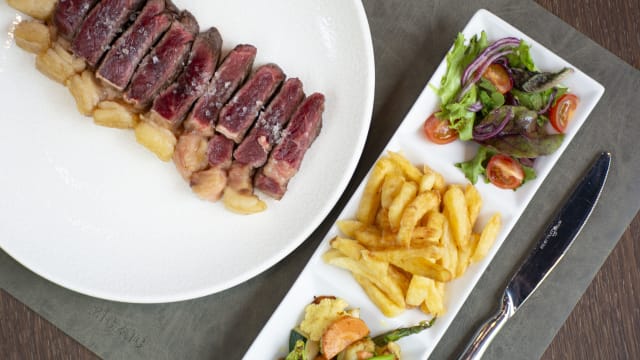 Ribeye de vaca rubia gallega acompañada de patatas fritas, wok de verduras y ensalada verde.