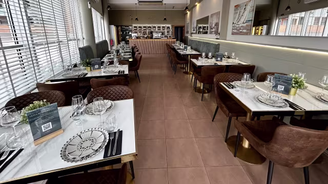 Interior moderno y elegante con mesas de mármol blanco y sillas marrón oscuro, creando un ambiente acogedor y cómodo.