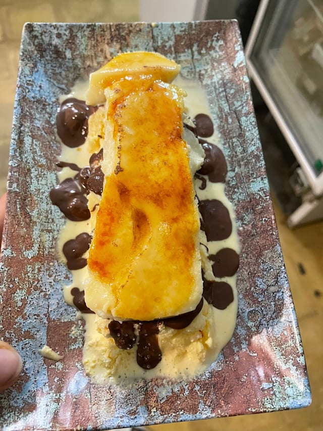 Postre de helado cremoso con plátano caramelizado, bañado en salsa de chocolate y servido sobre un bizcocho ligero.