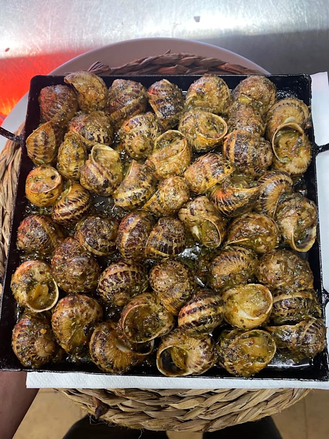 Caracoles a la parrilla con aceite de hierbas, adornados con perejil y ajo picados.