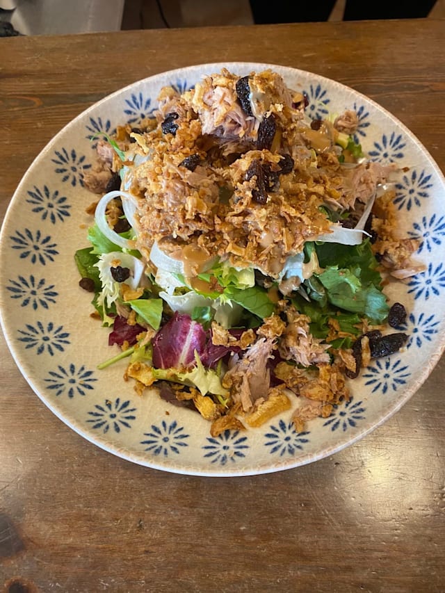Ensalada colorida con lechugas frescas, pollo desmenuzado, cebollas fritas crujientes y arándanos secos.