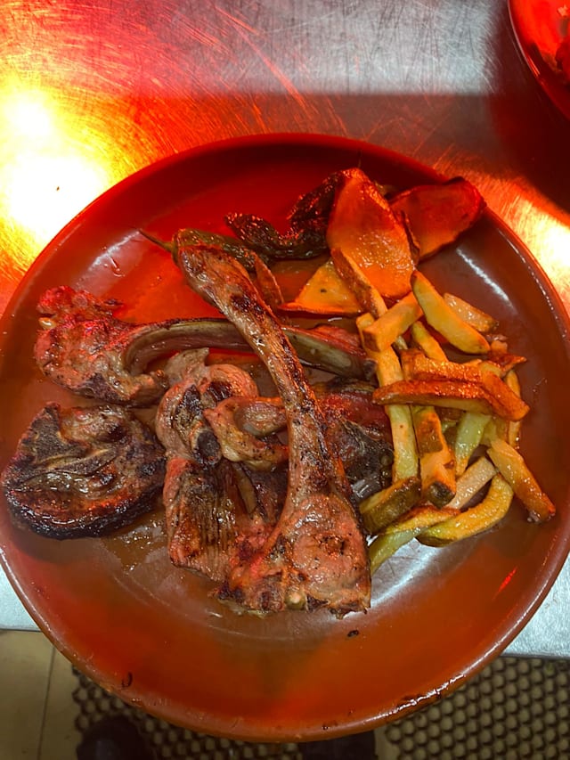 Selección de carnes a la parrilla, incluyendo chuletas de cordero ahumadas, acompañadas de papas asadas y verduras a la parrilla.