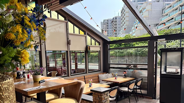 Het interieur van het restaurant is helder en uitnodigend, met grote ramen die natuurlijk licht binnenlaten. De decoratie combineert houten elementen met moderne meubels, wat een gezellige sfeer creëert. Er zijn verschillende tafels met comfortabele zitplaatsen. Het buitengedeelte is omgeven door groen, wat de algehele ambiance versterkt. Sfeervolle lichtjes hangen boven, wat een warme toets toevoegt. De ruimte is goed onderhouden en ideaal voor informele diners of sociale bijeenkomsten.