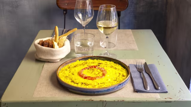 Paella con riso allo zafferano, gamberi succulenti, peperoni rossi e piselli, guarnita con erbe fresche.