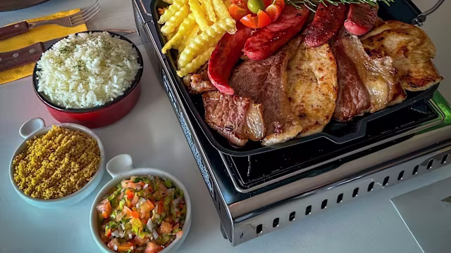 Prato generoso de carnes grelhadas, incluindo cortes de porco e vaca, acompanhadas de batatas fritas crocantes, fatias de chouriço e arroz branco. Inclui também molhos coloridos com tomate, cebola e ervas, e uma mistura de especiarias.