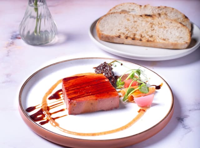 Smooth pâté garnished with pickled vegetables, drizzled with dark sauce, and accompanied by rustic bread and chopped herbs.