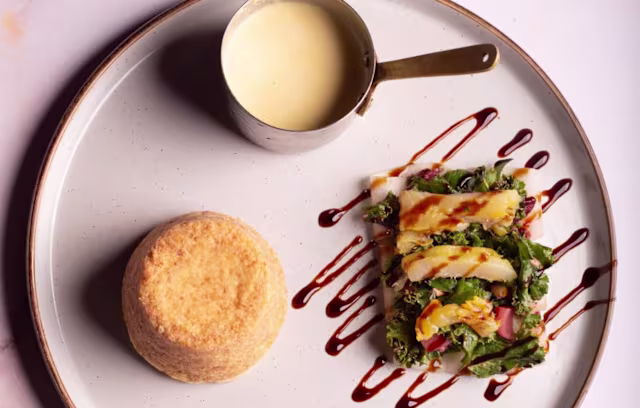 Fluffy golden-brown cake served with a fresh mixed greens salad topped with colorful vegetables and drizzled with balsamic reduction, accompanied by a creamy sauce.