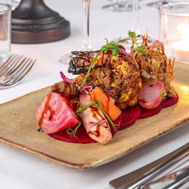 Chargrilled shrimp served with watermelon radish, beetroot purée, microgreens, and edible flowers, offering a balance of flavors and textures.