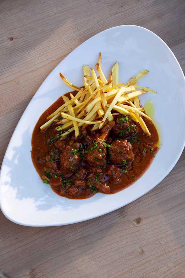 Albóndigas tiernas en una salsa rica y sabrosa, acompañadas de papas fritas crujientes.