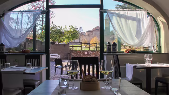 Interno di un ristorante con grandi finestre che offrono una vista serena, tavoli e sedie in legno, decor minimalista e atmosfera accogliente.