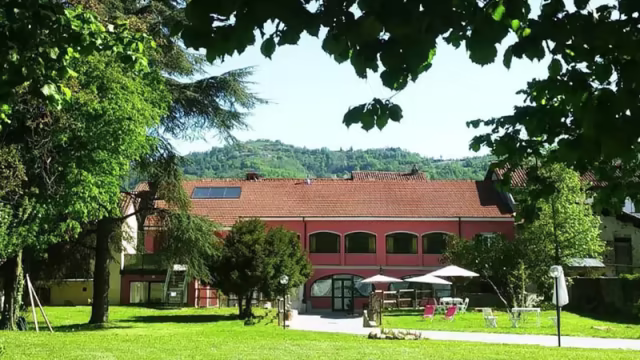 Ristorante immerso nel verde, con facciata rossa e tetto inclinato, tavoli all'aperto e colline sullo sfondo.