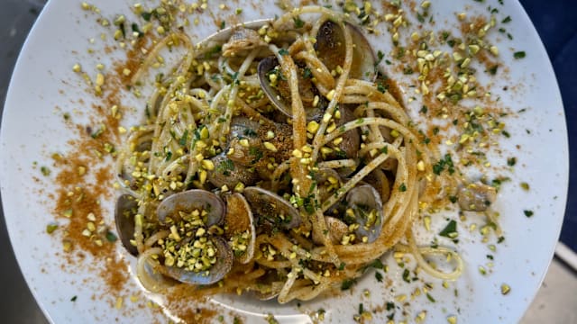 Spaghetto alle vongole veraci con granella di pistacchio e bottarga fresca Un grande classico rivisitato con gusto: spaghetto alle vongole veraci, saporito e profumato, arricchito dalla croccantezza della granella di pistacchio e dal carattere deciso della bottarga fresca grattugiata al momento. Un piatto che unisce mare e terra in un equilibrio perfetto di consistenze e aromi.