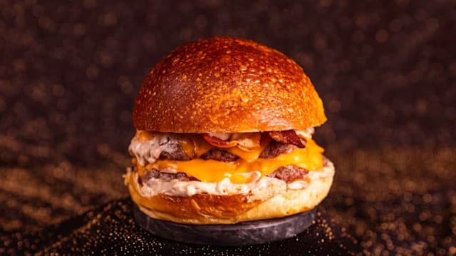 The Trufa Corp Doble smash dry aged de 100 gr cada disco, salsa trufada Gula, nube de parmesano, cebolla caramelizada y huevo frito