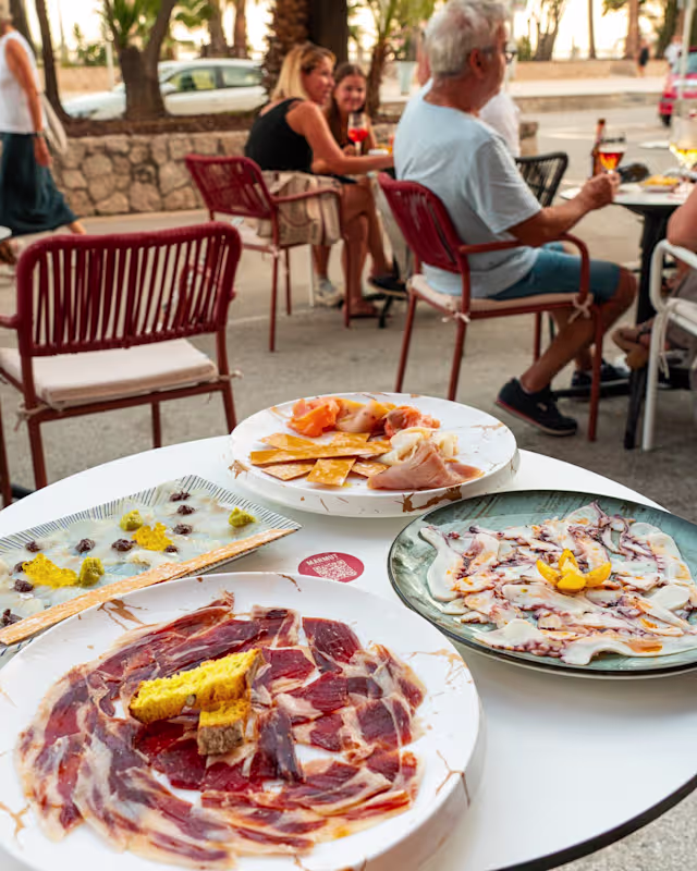 Platos de charcutería con jamón, salami y salmón ahumado, acompañados de rodajas de cítricos y mostaza.