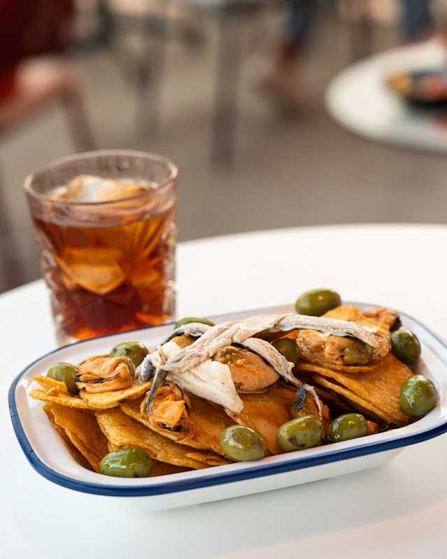 Nachos crujientes con queso derretido, aceitunas verdes y anchoas, ofreciendo un sabor salado y sabroso.