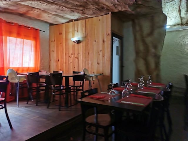 Interior de restaurante con paredes de piedra natural y particiones de madera rústica, iluminado con luz suave y mesas decoradas con manteles rojos.
