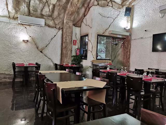 Interior rústico con paredes de piedra texturizada, mesas y sillas de madera oscura, y una atmósfera acogedora.