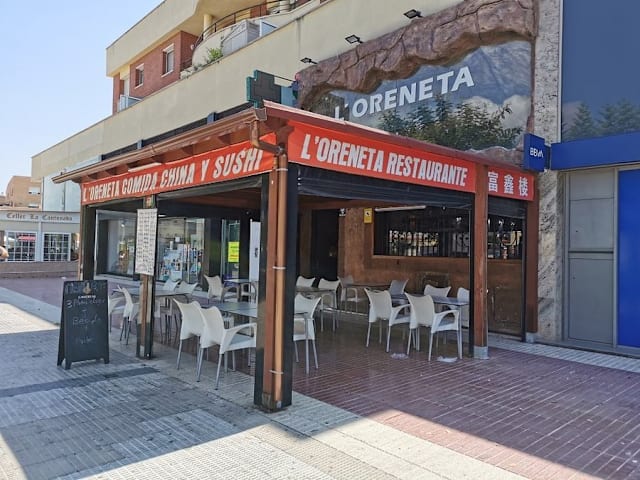 Fachada moderna del restaurante L'Oreneta, con toldo rojo, asientos al aire libre y un ambiente acogedor.