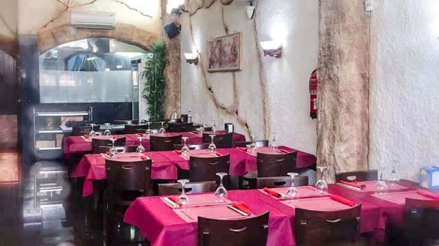 Interior acogedor con mesas cubiertas de mantel rojo, sillas de madera elegantes y una iluminación suave que realza la decoración rústica.