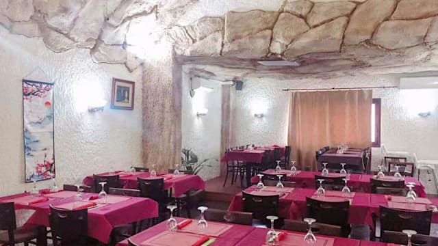 Interior del restaurante con diseño de cueva, paredes rocosas texturizadas, manteles rojos brillantes y una atmósfera acogedora.
