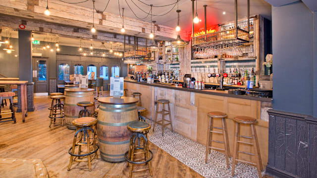 A stylish bar interior with wooden barrels, high stools, warm pendant lighting, and a variety of spirits, blending rustic charm with contemporary design.