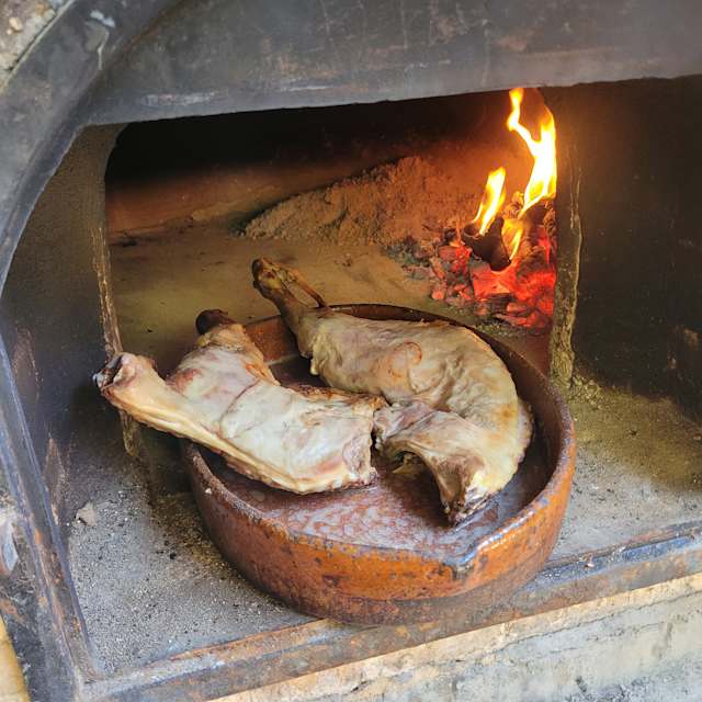Cortes de carne a la parrilla, probablemente cordero o cerdo, con una costra dorada y sabor ahumado, preparados en un horno de leña.