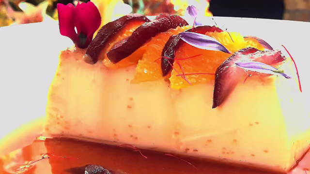 Postre cremoso y suave, similar a un flan o panna cotta, decorado con rodajas de naranja, salsa de caramelo y flores comestibles.